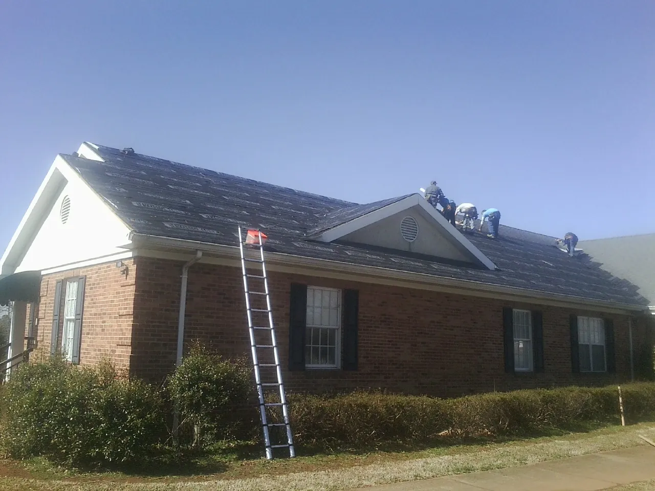 Crew tearing shingles off a brick ranch roof with a ladder set — Emergency Roof Repair work by our crew in Rye