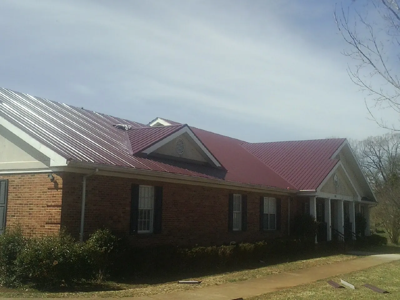 Red metal roof with gabled entries on a long brick building, from a Hail Damage Roof Repair job in Rye