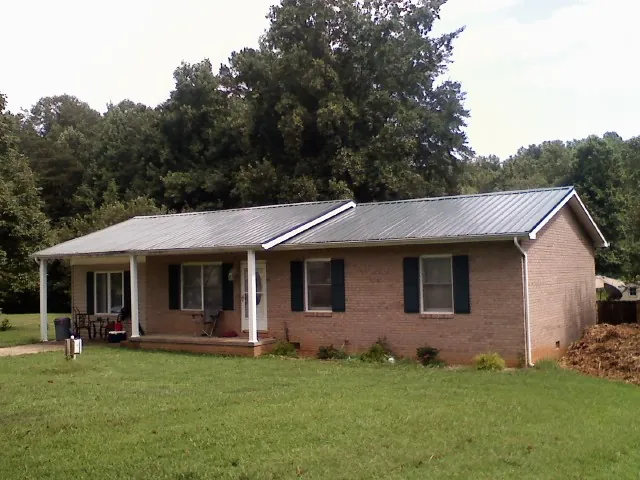 Gray metal roof on a brick ranch house with a side carport in Rye