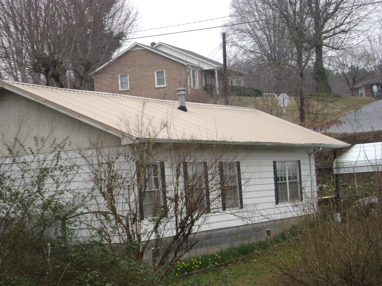 Tan metal roof on a white sided house set into a hillside — Commercial Roofing by Roofing Brothers in Rye